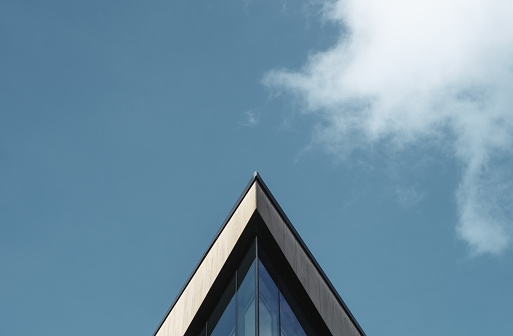 Abstract Architectural Image Of A Triangular Building Against A Blue Sky WIth Clouds And Copy Space