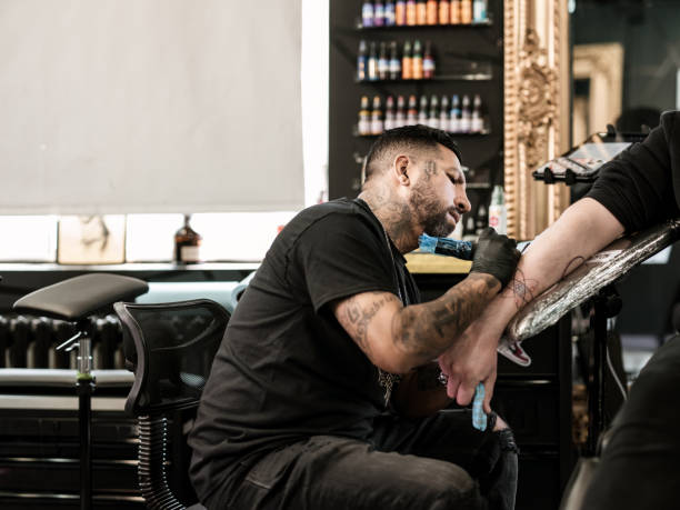 istock Mexican male Tattoo artist creating art on client arm 1395032009