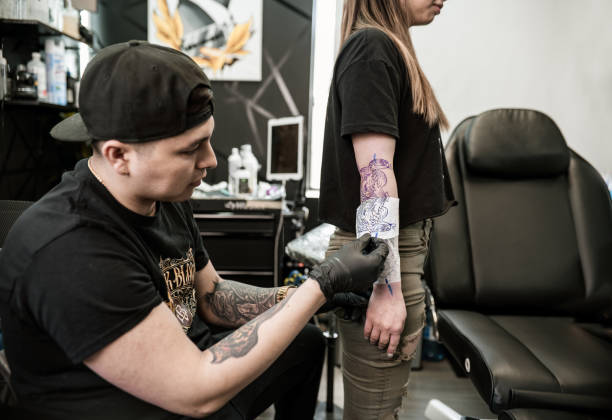 istock Mexican male Tattoo artist creating art on client arm 1395033341