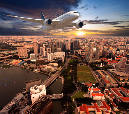 White passenger plane in flight during the sunset. Aircraft  flies above the skyscrapers of the business center of the big city. Front view of aircraft.