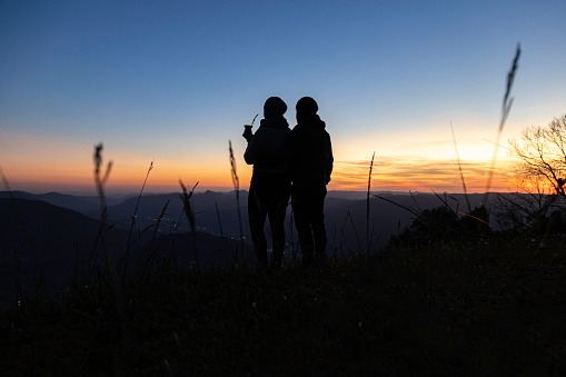 Silhouette of a couple with a yerba mate drink looking at the sunset on the top of a mountain, in Rio Grande do Sul highlands, Brazil