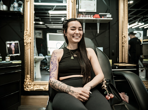 Young Asian woman at the tattoo parlour. She is wearing casual clothes. Interior of tattoo parlour during day.