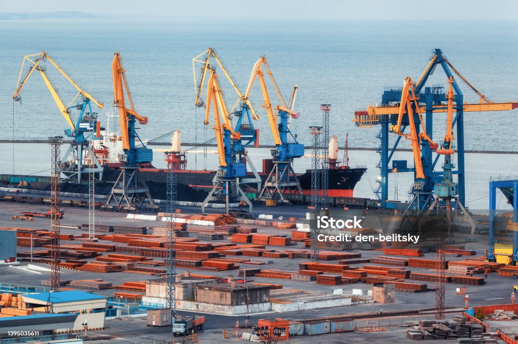 Sea commercial port at night in Mariupol, Ukraine before the war. Industrial. Cargo freight ship with working cranes bridge in sea port at twilight. Cargo port, logistic. Heavy industry Mariupol Stock Photo