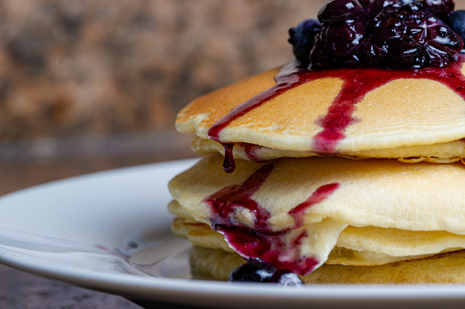 a stack of homemade pancakes topped with fresh blueberries and blueberry syrup.