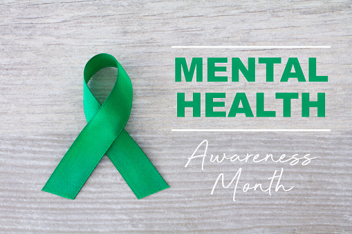 Mental Health Awareness Month  written on a  light wooden background, with a green ribbon.