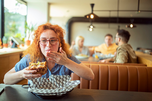 A hungry redhead woman enjoys a delicious burger at a fast food restaurant.