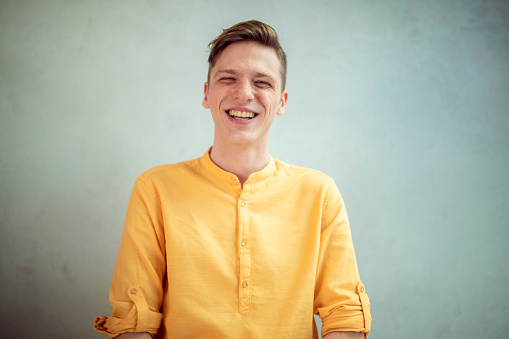 A picture from the waist up of a man in a yellow blouse with a wide smile on his face.