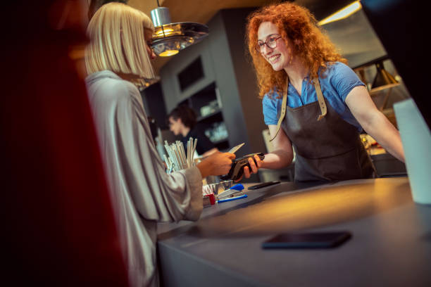 Redhead waitress holds POS terminal for female customer in coffee shop for credit card payment. stock photo