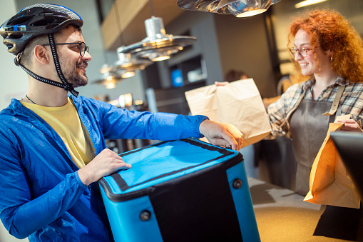 A smiling food delivery man picks up ordered food from a waitress at a fast food restaurant.