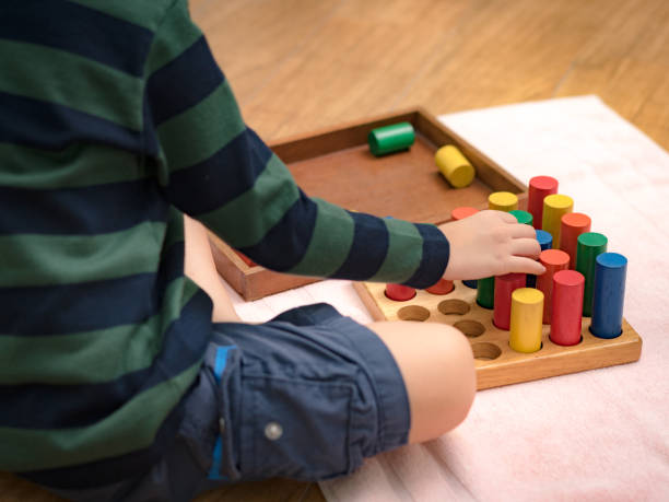 istock Montessori preschool student's hand  learning and playing with wooden cylinder socket. 1395042608