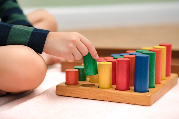 istock Montessori preschool student's hand  learning and playing with wooden cylinder socket. 1395042610