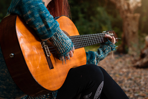 Young woman playing guitar in a forest, an autumn day. Autumn day. Woman playing a string instrument. Woman in the forest. Woman's hands playing guitar. Copyspace.