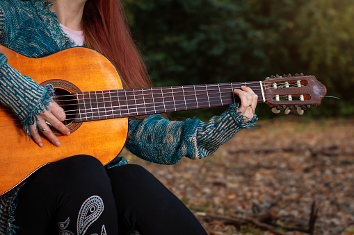 Young woman playing her guitar on a fall afternoon. Autumn afternoon. Young woman playing guitar. Young woman playing guitar in the forest
