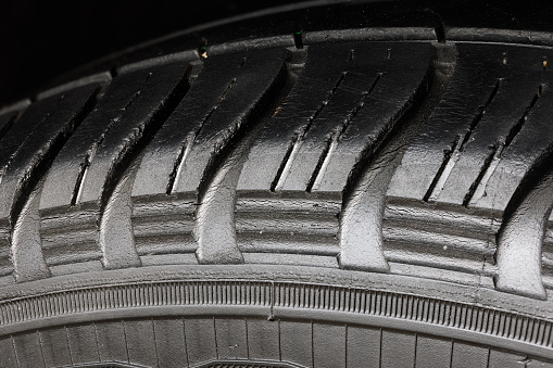 Old worn black tire with many large cracks in the car wheel. High magnification macro view.