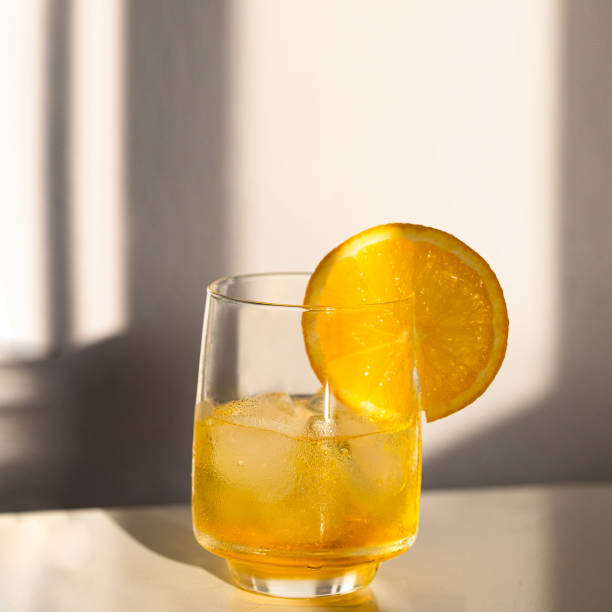 istock Summer cocktail with ice cubes  and orange slice on beige background with hard light and shadow. 1395046273