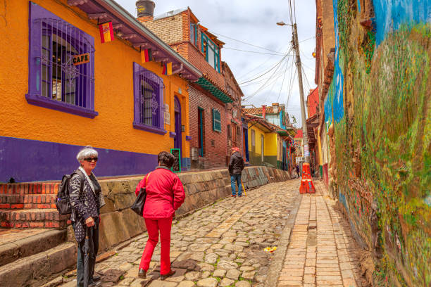 Bogotá, Colombia - Local Colombians on the Narrow, Cobblestoned Calle del Embudo In The Historic La Candelaria District of the Andes Capital City Bogotá, Colombia - July 20, 2016: Some local Colombians seen on the broader end of the, colourful, cobblestoned Calle del Embudo which is at the opposite end of the Plaza del Chorro de Quevedo. The Street gets its name from its funnel shape: Embudo translates to Funnel in English. It is shaped like a funnel. It must be remembered that these streets were set up over 450 years ago when people usually travelled on horseback. The Street is well known for its Street Art, many of which feature the legends of the Pre-Colombian era. Photo shot in the late afternoon sunlight; horizontal format. calle del embudo stock pictures, royalty-free photos & images