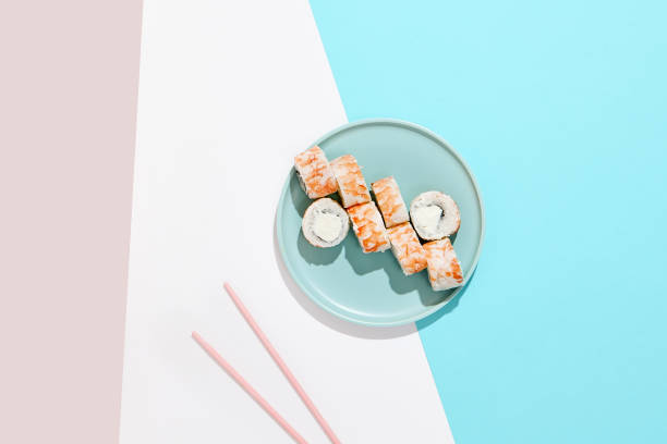 Maki roll with shrimp on ceramic plate with chopsticks. Shrimp sushi roll with philadelphia cheese on coloured background. Japanese menu concept. Prawn sushi roll in modern style.
