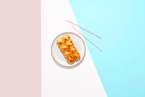 Hot maki roll with cheese on coloured background. Baked sushi roll with salmon inside, rice outside, cheese topped. Maki sushi in minimal style. Japanese menu concept.