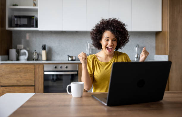 Excited woman at home working on her laptop and winning something Excited Latin American woman at home working on her laptop and winning something online - success concepts excitement laptop stock pictures, royalty-free photos & images