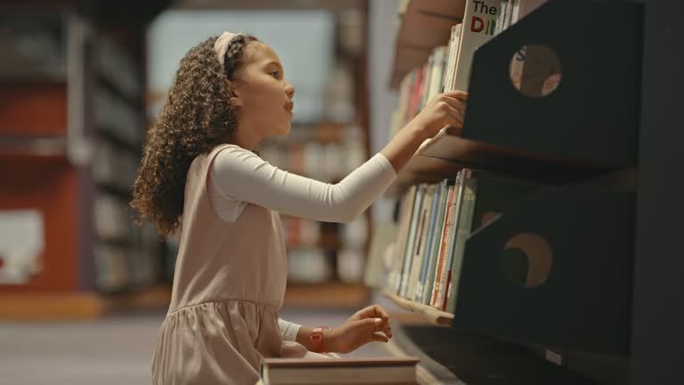 Little girl alone in a library. Young child doing research. Cute child doing her school work in a library.