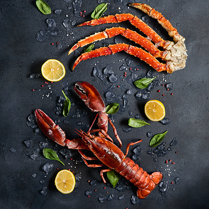 Lobster and crab legs with ice and lemon on dark background top view. Delicatessen crab and lobster seafood on black slate table. Crustacean seafood aesthetics. Luxury food - alive lobster and crab legs