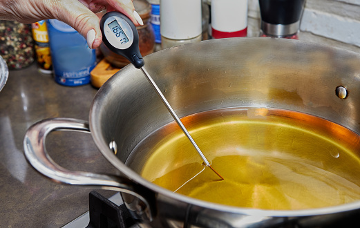 Chef checks the temperature of the heated oil in pot on gas stove with thermometer.
