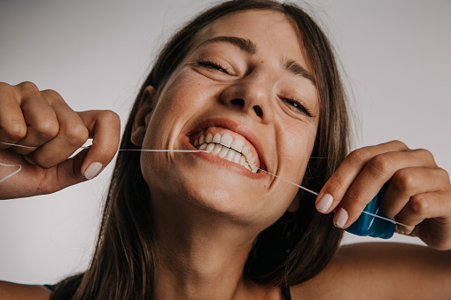 Oral Hygiene And Health Care Concept. Portrait of smiling confident Caucasian woman using dental floss, isolated over studio background.