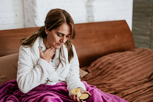 latin ill senior matured woman sneezing and using napkin for flu on bed at home in Mexico Latin America
