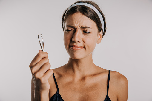 Shot of an attractive young woman in pain plucking her eyebrows against a studio background.