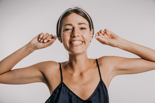 Shot of a young smiling woman cleaning her ear with an earbud against the studio background. Healthcare and ear cleaning concept
