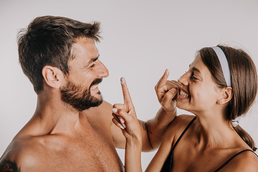 Shot of a happy young woman applying moisturiser on her husband’s face during their morning routine at home.