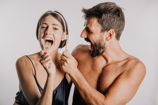 Happy lovely couple brushing their teeth together with toothbrush standing isolated on a studio background.