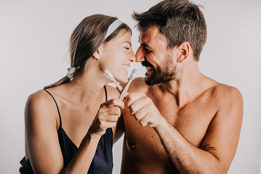 Happy lovely couple brushing their teeth together with toothbrush standing isolated on a studio background.