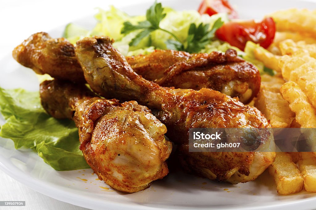 Plate of grilled chicken drumsticks, fries and salad Grilled chicken drumsticks, French fries and vegetables  Barbecue - Meal Stock Photo