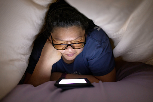 High quality stock photo of a woman using an e-reader under the covers.