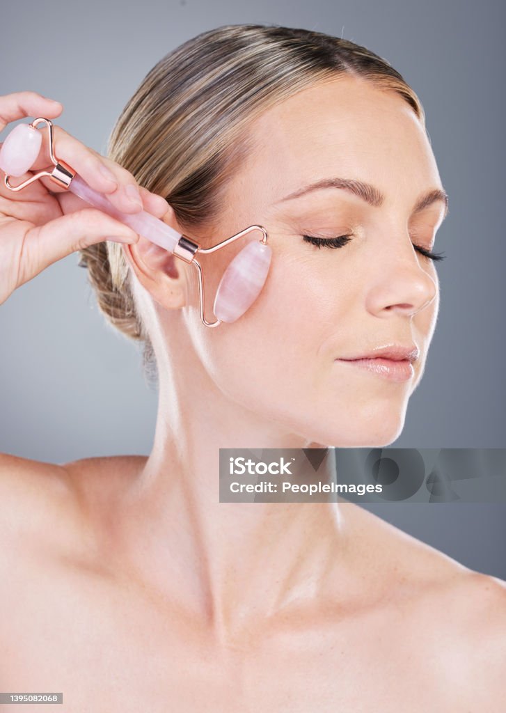Studio shot of an attractive mature woman using a rose quartz roller on her face against a grey background Keeping her skincare routine on a roll Rose Quartz Stock Photo