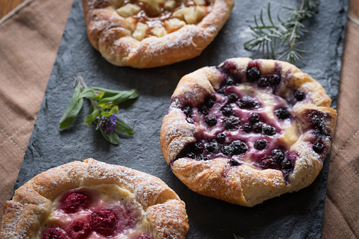 Farm to table - freshly baked apple, blueberry and raspberry custard danishes dusted with icing sugar and served on a slate platter.  Vancouver, British Columbia, Canada