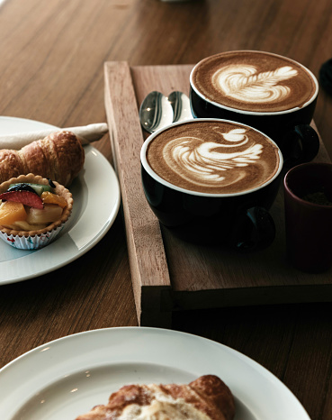 Bakery with coffee and croissants in a wooden tray on the table.