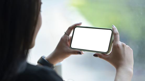 View over shoulder of young woman holding smart phone in horizontal position. Empty screen for advertising text.