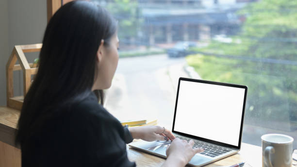 istock Rear view young woman using computer laptop while sitting near window in office with view of city district. 1395088618
