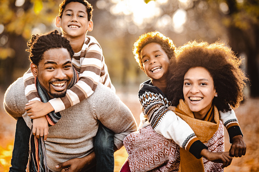 Happy African American family having fun while piggybacking in autumn day at the park.