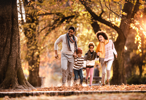 Happy African American family having fun while holding hands and running in autumn day outdoors.