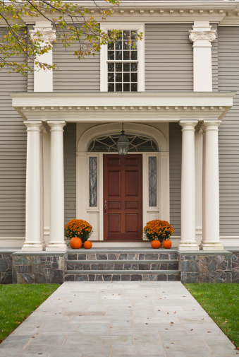 Wood Front Door and Entrance with Columns and Twin Flowerpots flanking door. Also 4 pumpkins, 2 on each side of the door. Shows walkway and 3 steps up to entrance. Shows second storey window above door.