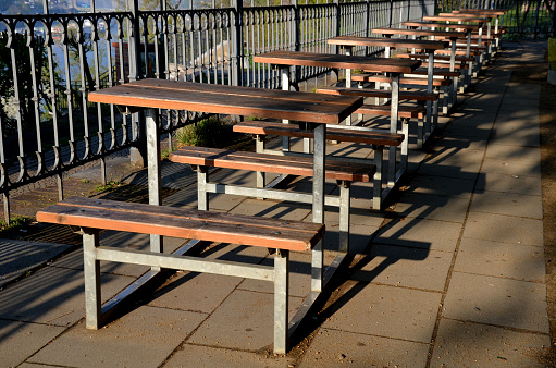 wooden seating area with benches lined with natural wood by the water. terrace by the pond with a picnic bench and old round tables as in a cafe. terrace steel railing