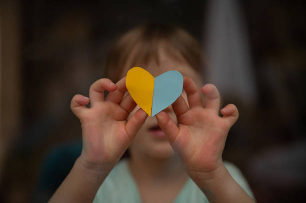 Little toddler child holding a heart shaped paper in the colors of ukrainian flag stock photo