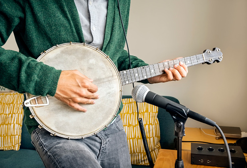 Close-up of a man playing the banjo into a microphone in his home recording studio