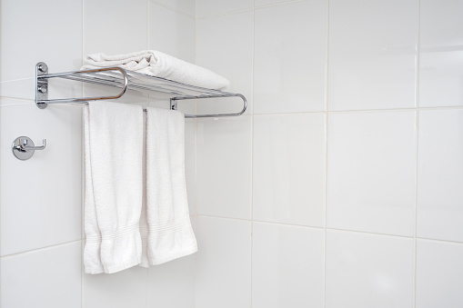 Interior of bathroom with iron shelf and soft towels. White tiles with minimal composition in bathroom.