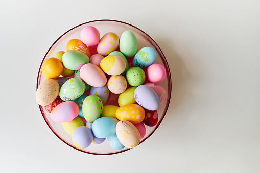 A pink bowl of brightly colored decorated Easter eggs on a light gray table