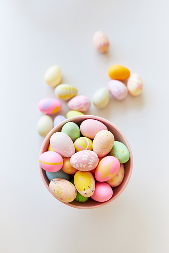 A pink bowl of brightly colored decorated Easter eggs on a light gray table