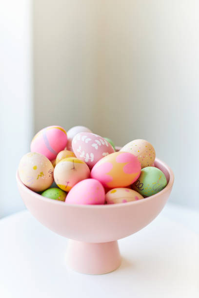 A pink bowl of brightly colored decorated Easter eggs on a light gray table